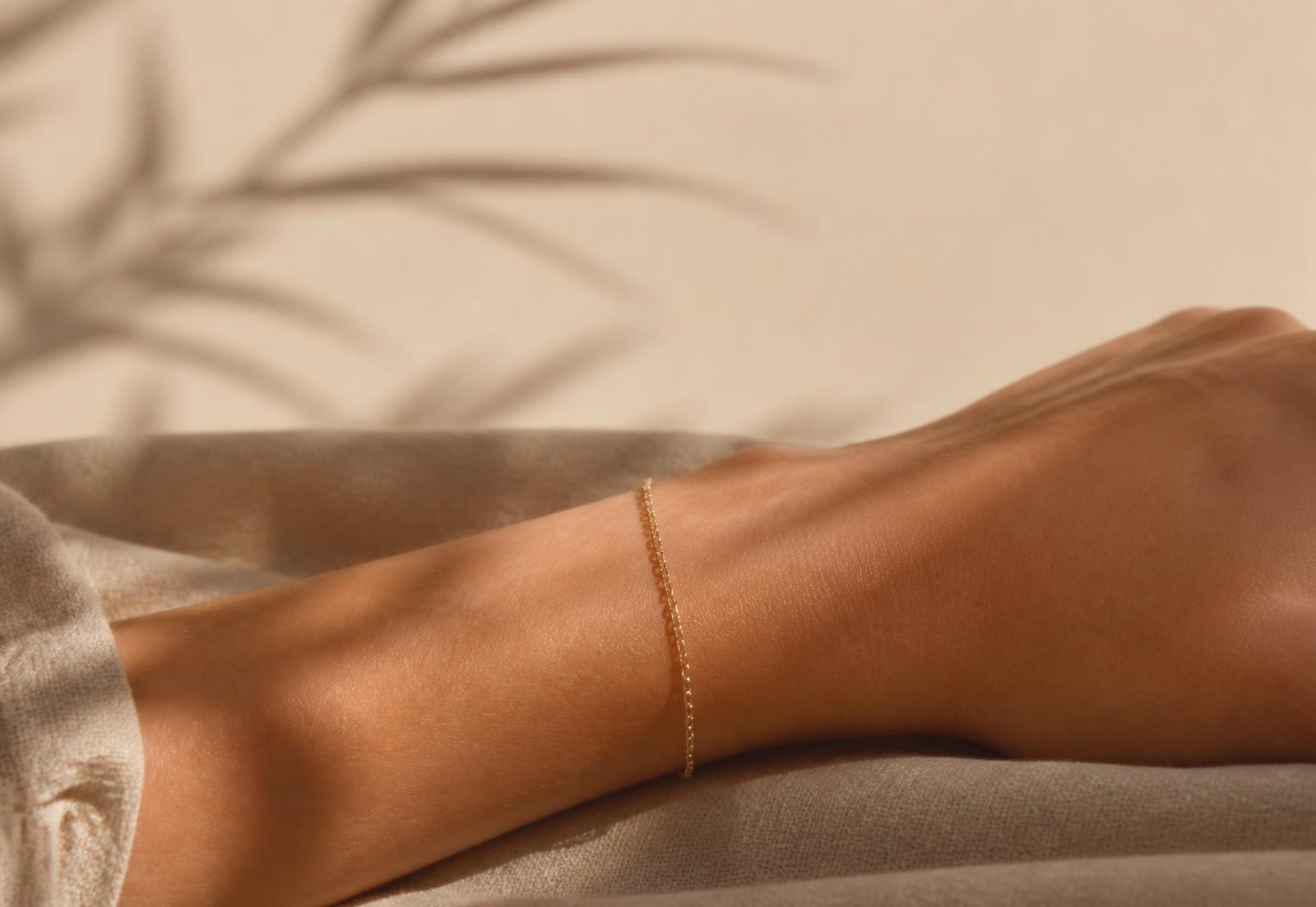 Fine gold permanent bracelet welded on a wrist resting on champagne linen